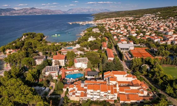 Scenic aerial view of a coastal town with red roofs, lush greenery, and clear sea.