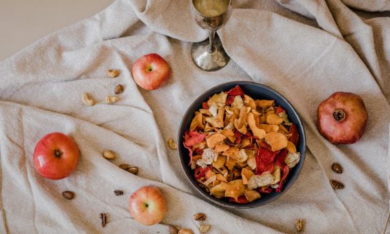Overhead view of a bowl of dried fruit with apples, nuts, and a silver goblet on a rustic fabric.